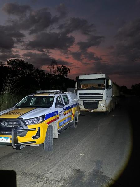 Veículo da Polícia Militar Rodoviária parado ao lado de um caminhão em um cenário noturno com céu avermelhado.