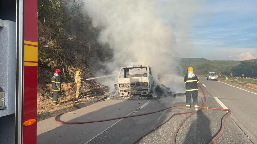 Bombeiros combatendo incêndio em caminhão na BR 262, com fumaça e chamas visíveis.