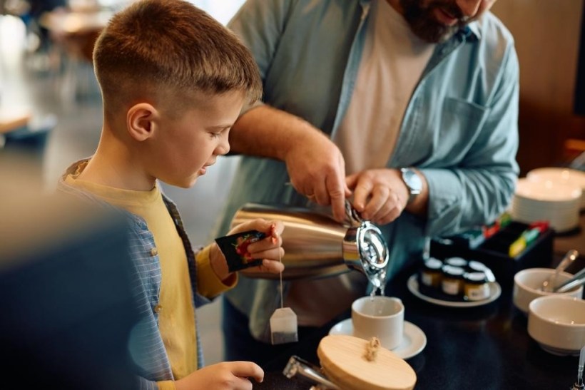 Criança e adulto preparando chá juntos em uma mesa de café da manhã.
