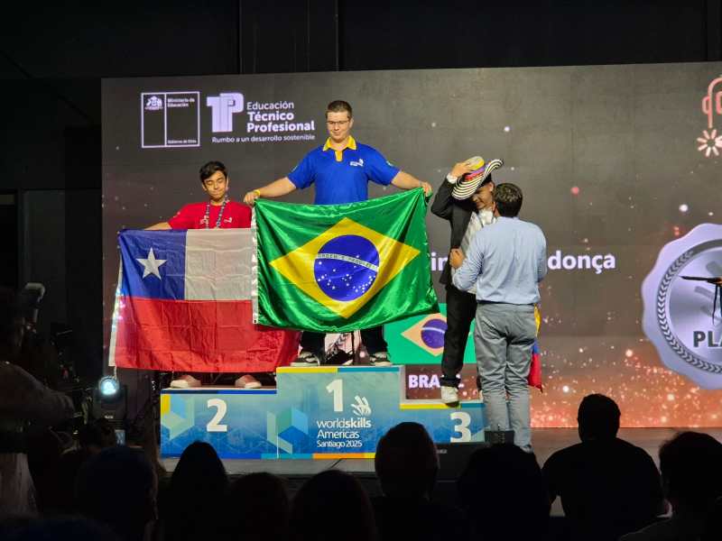 Evento de premiação da WorldSkills Américas 2023, com competidores segurando as bandeiras do Brasil e do Chile no pódio.
