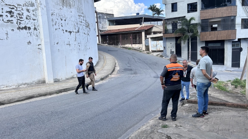 Grupo de pessoas discutindo em uma rua, próximo a um muro que apresenta sinais de deterioração, em Divinópolis.