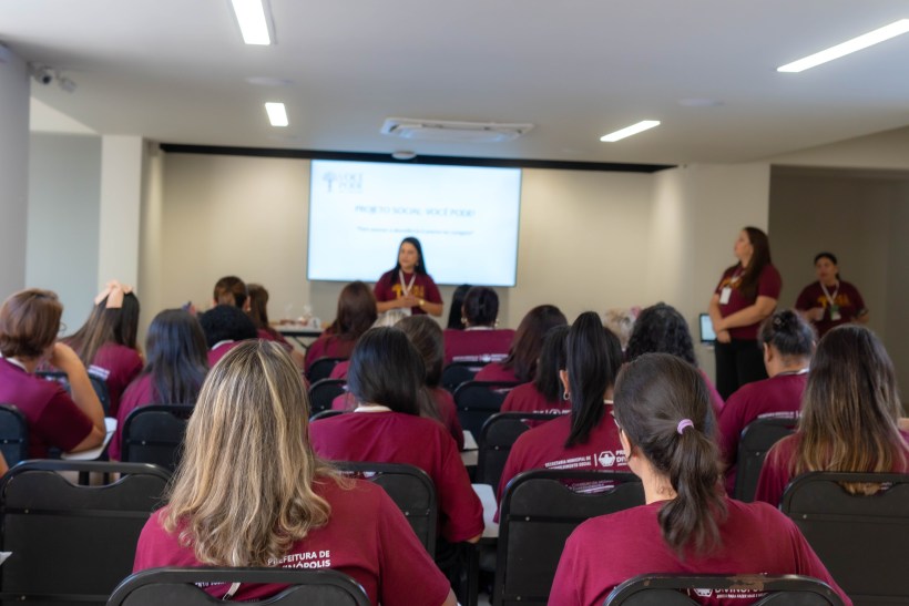 Evento de encerramento do Projeto Social 'Você Pode', com mulheres empreendedoras em um auditório, assistindo a uma apresentação no palco.