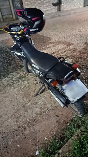 Motocicleta preta estacionada em uma rua, vista de trás, com capacete no guidão.