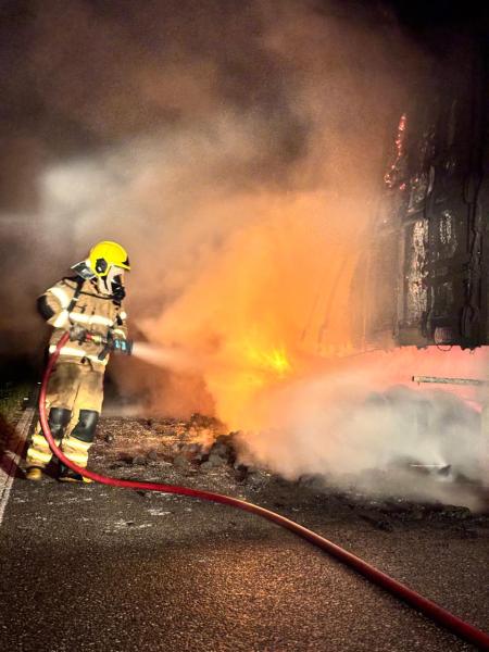 Bombeiro combatendo incêndio em uma carreta na rodovia BR-354, com chamas e fumaça visíveis.