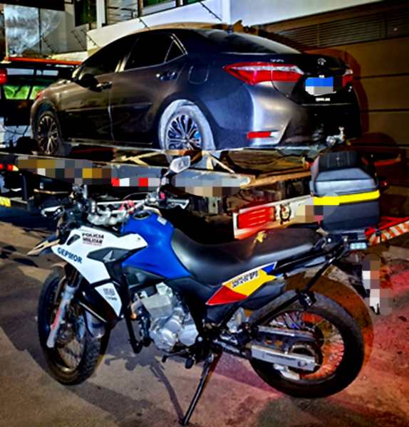 Uma motocicleta e um veículo estacionados em um reboque, com foco na operação policial de apreensão de veículos com irregularidades.
