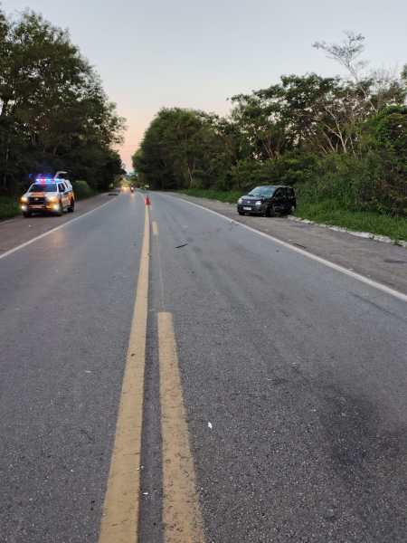 A view of a deserted road lined with trees, featuring a police vehicle with flashing lights on the left side and a parked black car on the right.