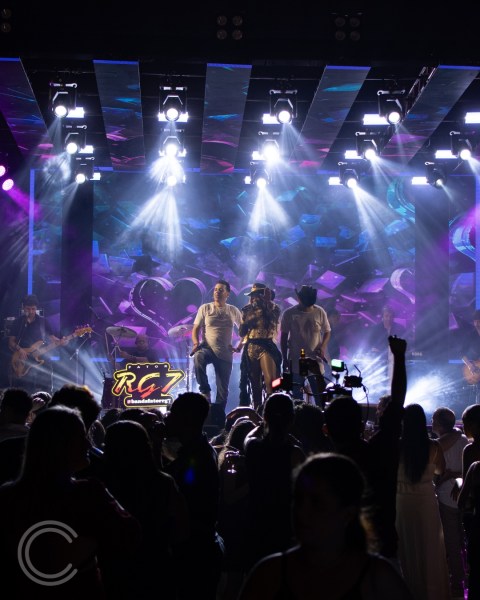 Show ao vivo da banda RG7 durante evento de confraternização, com luzes coloridas e público animado na plateia.