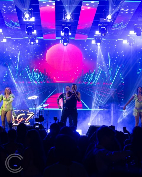 Apresentação animada no palco da festa Celebrar 2.0, com cantores e dançarinas em destaque, sob luzes vibrantes e um cenário festivo ao fundo.