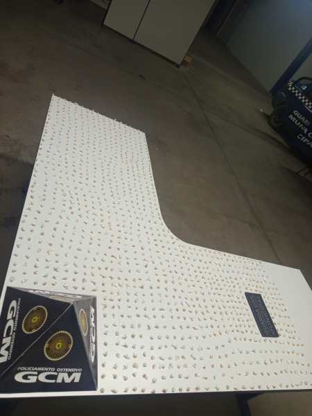 Imagem de uma mesa de atendimento ou exibição da Guarda Civil Municipal, com um design moderno e superfície branca com detalhes em formato de pontas ou correntes, indicando segurança ou identificação da entidade.