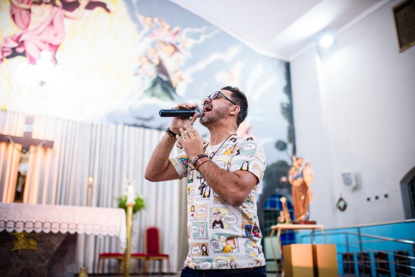 Homem cantando em um ambiente de adoração com altar ao fundo, retratando um momento de oração espiritual.