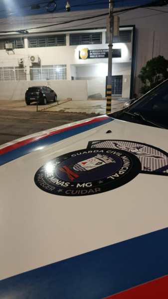 Visão da parte superior de um carro da Guarda Municipal, destacando o emblema e a cor característico, com um fundo de um prédio da prefeitura à noite.