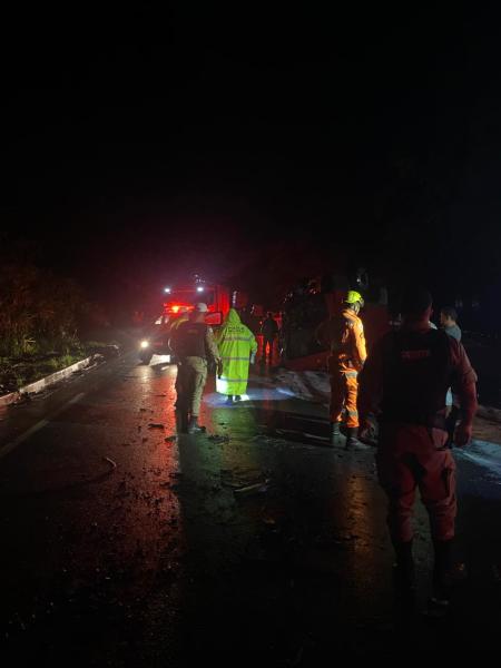 Cenário noturno de um acidente na estrada, com bombeiros e equipes de resgate trabalhando no local, cercados por veículos de emergência e iluminação.