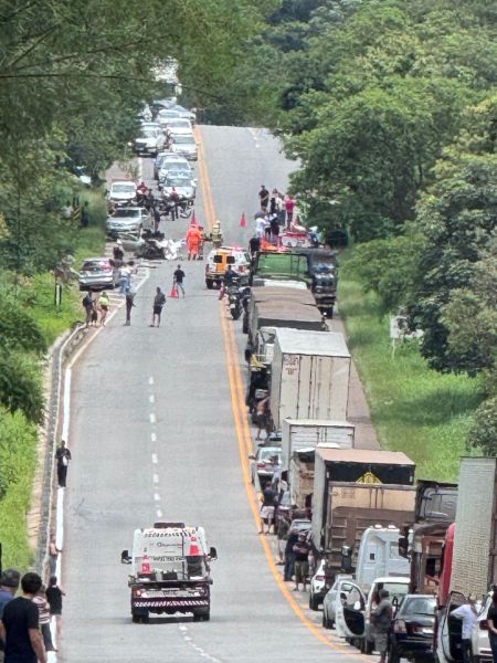 Uma longa fila de veículos e caminhões em uma estrada, com pessoas nas laterais, possivelmente participando de um protesto ou manifestação.