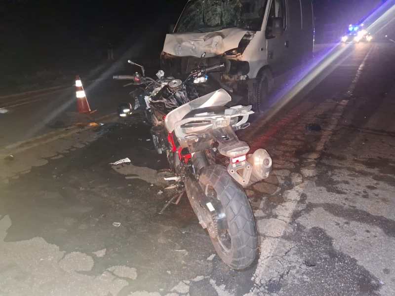 Motocicleta danificada ao lado de uma van acidentada em uma estrada, à noite.