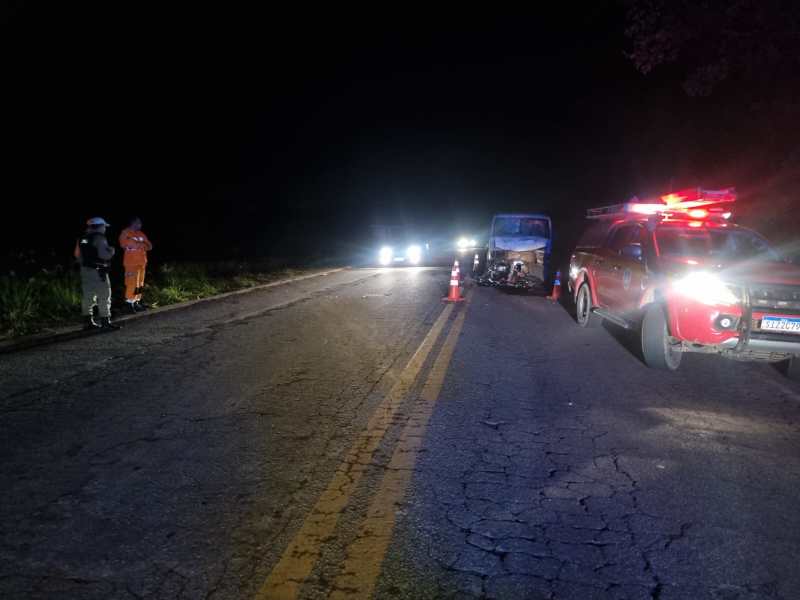 Cena noturna de um acidente de trânsito com veículos parados na estrada, incluindo uma viatura de emergência com luzes piscantes e cones de sinalização.