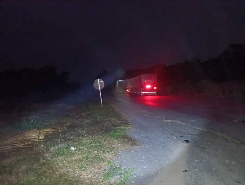Caminhão se afastando em uma estrada rural escura à noite, com um sinal de trânsito visível ao lado.