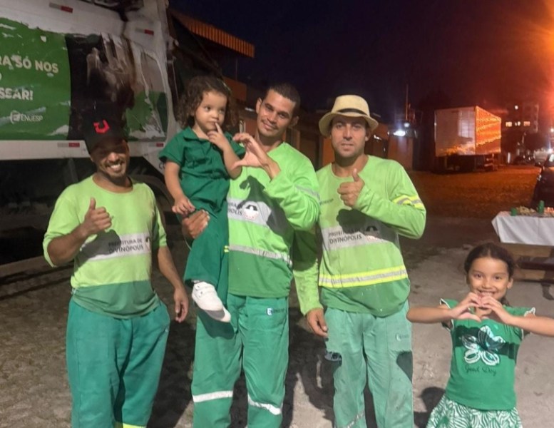 Quatro pessoas sorridentes em um ambiente noturno, vestindo uniformes verdes, com duas crianças no centro fazendo gestos de coração, enquanto adultos mostram sinal de positivo.