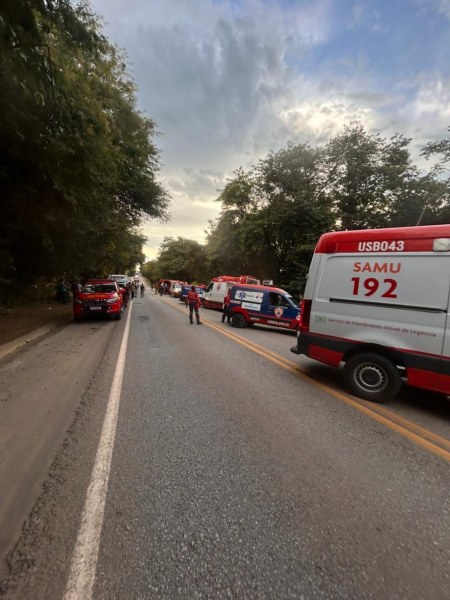 Caminho com várias ambulâncias do SAMU 192 estacionadas ao lado, com pessoas próximas em um ambiente arborizado.