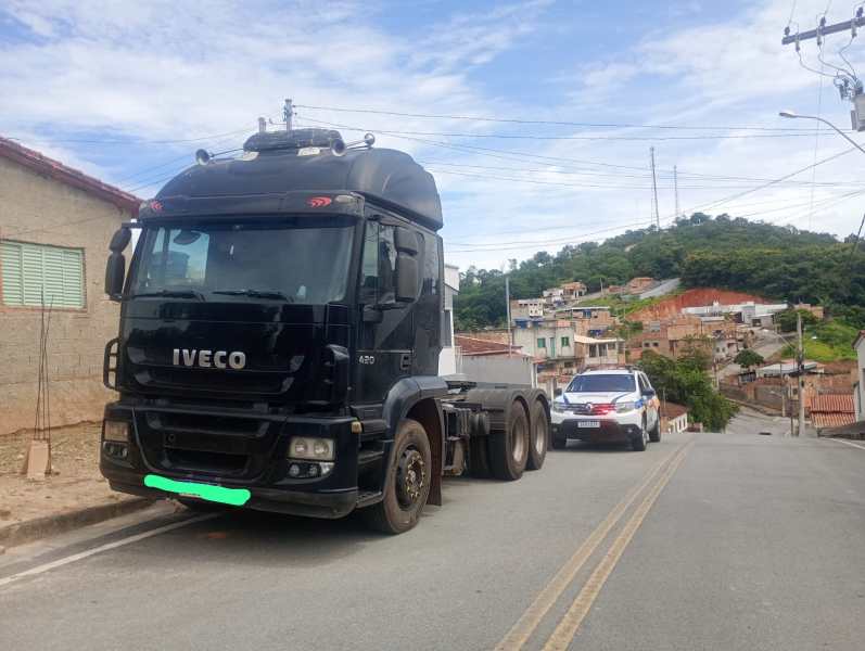 Caminhão Iveco preto estacionado em uma rua com casas ao fundo.
