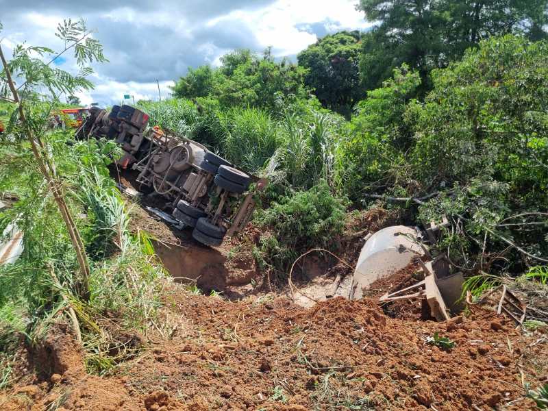 Caminhão acidentado deitado em um barranco com vegetação ao redor.