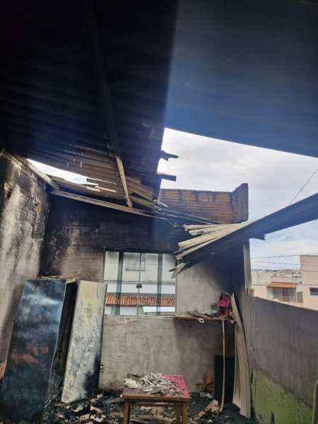 Interior de uma sala com danos significativos, incluindo um teto quebrado e paredes chamuscadas, evidenciando os efeitos de um incêndio.