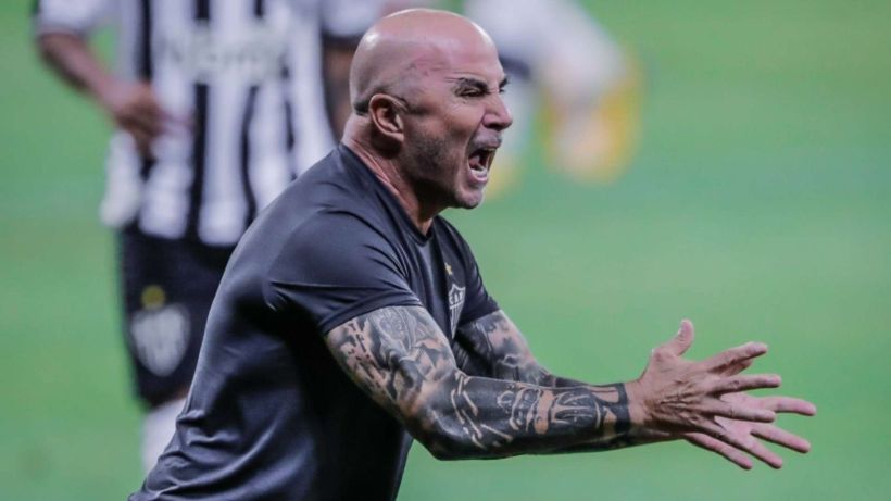 A coach passionately gesturing and shouting on the sidelines during a soccer match.