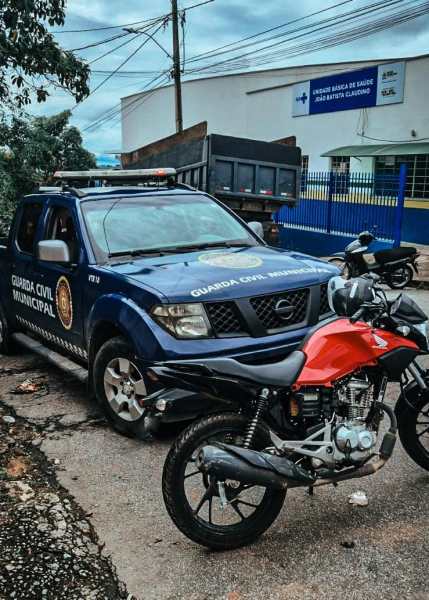 Uma viatura da Guarda Civil Municipal estacionada ao lado de uma moto vermelha, em uma rua urbana.