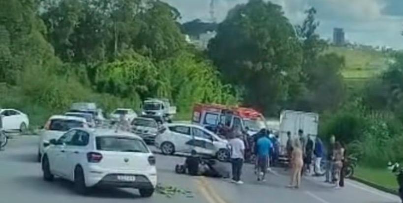 Acidente de trânsito envolvendo vários veículos, com pessoas prestando ajuda e uma ambulância na cena.