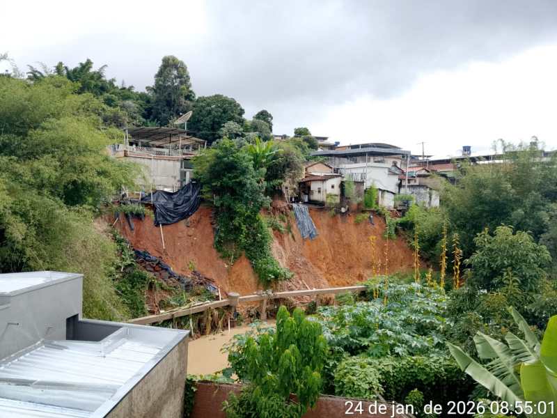 Vista de um deslizamento de terra em uma área urbana, com casas em risco e vegetação ao redor.
