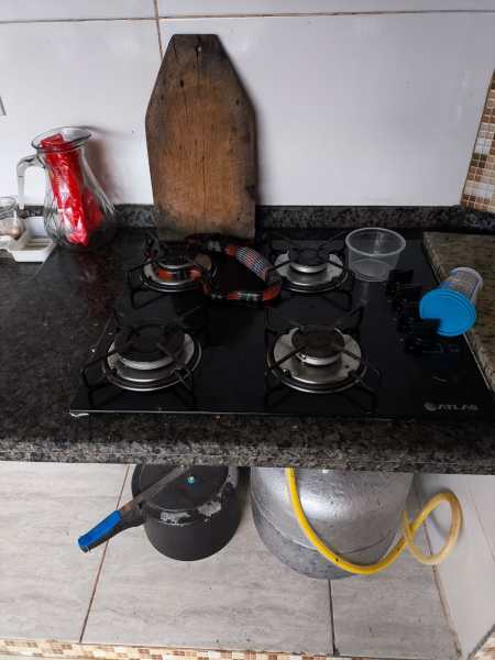 Fogão a gás com quatro bocas, panela sobre a mesa, garrafa de vidro e utensílios ao fundo.