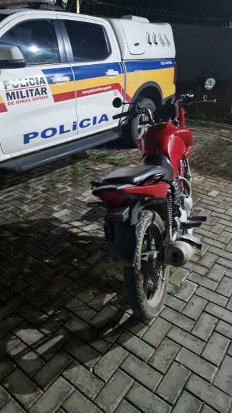 Uma motocicleta vermelha estacionada ao lado de uma viatura da Polícia Militar de Minas Gerais durante a noite.