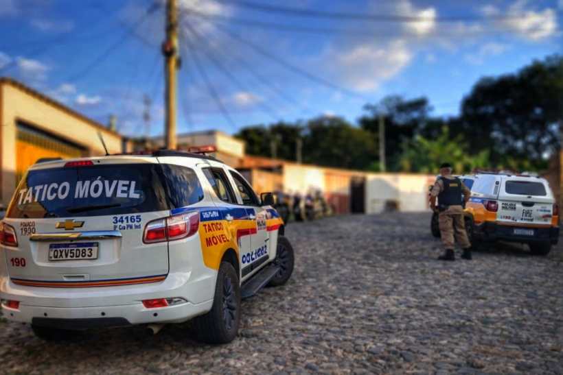 Viatura da polícia tática em uma rua de paralelepípedo, com agentes de segurança ao fundo.