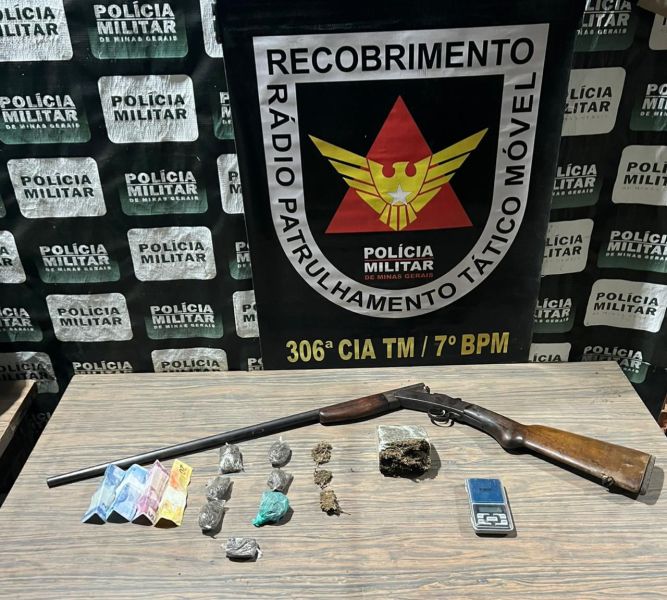 Uma espingarda de cano duplo, diversas substâncias suspeitas embaladas em pequenos saquinhos coloridos, alguns pedaços de material, uma balança e um fundo com a logo da Polícia Militar.