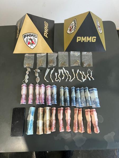 Imagem de objetos apreendidos, incluindo pacotes com substâncias, dinheiro em cédulas, e dois chapéus da PMMG (Polícia Militar de Minas Gerais) em destaque.