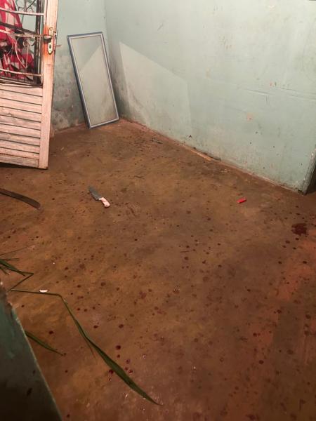 Interior de um ambiente com piso de cimento manchado de sangue, um espelho encostado na parede e alguns objetos espalhados pelo chão.
