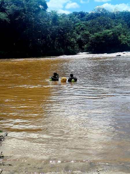 Duas pessoas em trajes de mergulho nadando em um rio de água turva, cercado por vegetação.
