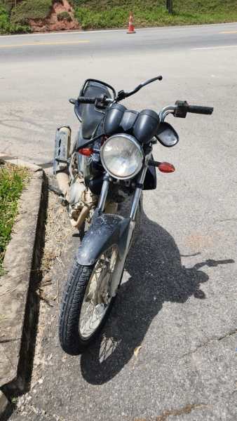 Uma motocicleta preta estacionada na calçada, com vista lateral e dianteira, em uma estrada.