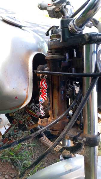 Detalhe de uma motocicleta mostrando o tanque, cabos e componentes do motor.