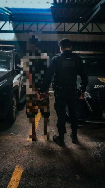 Um policial segurando a mão de uma pessoa em um estacionamento, com veículos ao fundo.