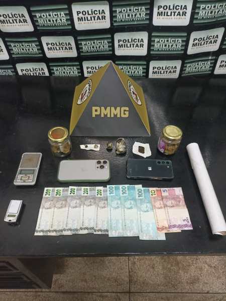 Imagem de itens apreendidos pela polícia, incluindo dinheiro em notas, celulares, balança, frascos e uma pirâmide com a sigla PMMG ao fundo.