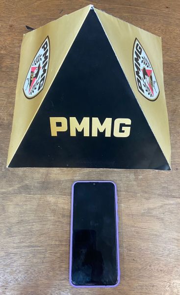 Um boné em formato de pirâmide com a sigla PMMG em destaque e um celular preto na parte inferior da imagem.