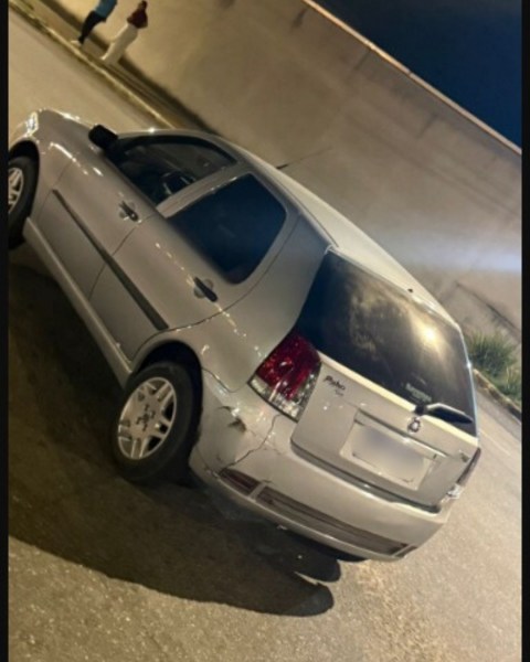 Um carro hatchback prateado estacionado à noite, com uma parte traseira ligeiramente danificada.
