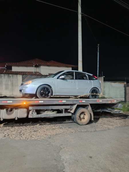 Um carro cinza estacionado em cima de um reboque à noite, com casas ao fundo.