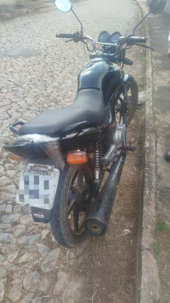 Moto preta estacionada em uma rua de paralelepípedos, vista lateral.