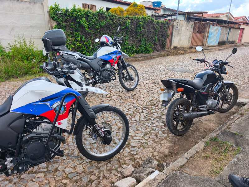 Duas motocicletas com cores azul e vermelha estacionadas em uma rua de paralelepípedos, com uma terceira moto preta em primeiro plano.