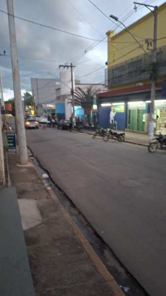 Rua em um bairro urbano, com lojas à direita e motocicletas estacionadas, iluminação crepuscular.