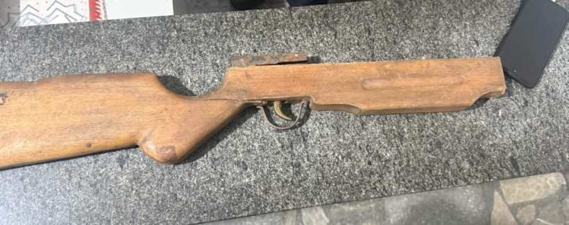 Um rifle de madeira repousando sobre uma superfície de pedra escura.