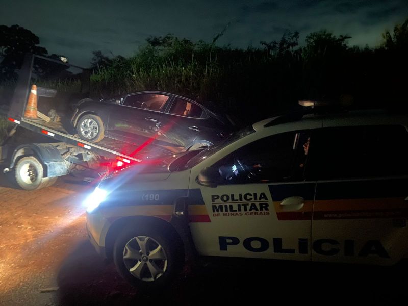 Veículo sendo rebocado por uma caminhonete da polícia militar à noite em uma área rural.