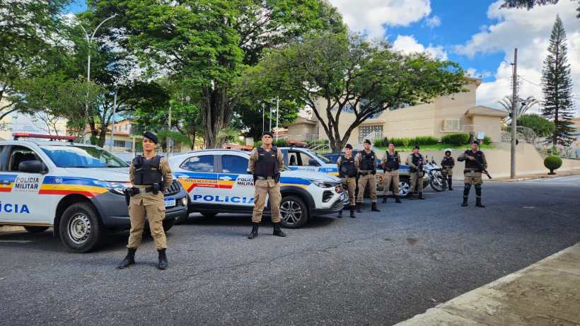 Grupo de policiais militares em frente a viaturas estacionadas em uma rua arborizada.