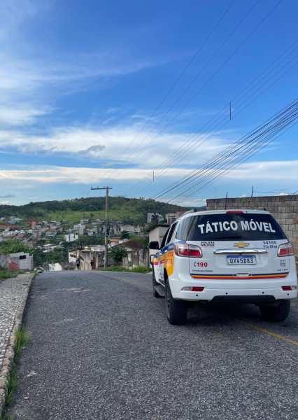Veículo de polícia com a inscrição 'TÁTICO MÓVEL' estacionado em uma rua em uma área residencial com colinas ao fundo.